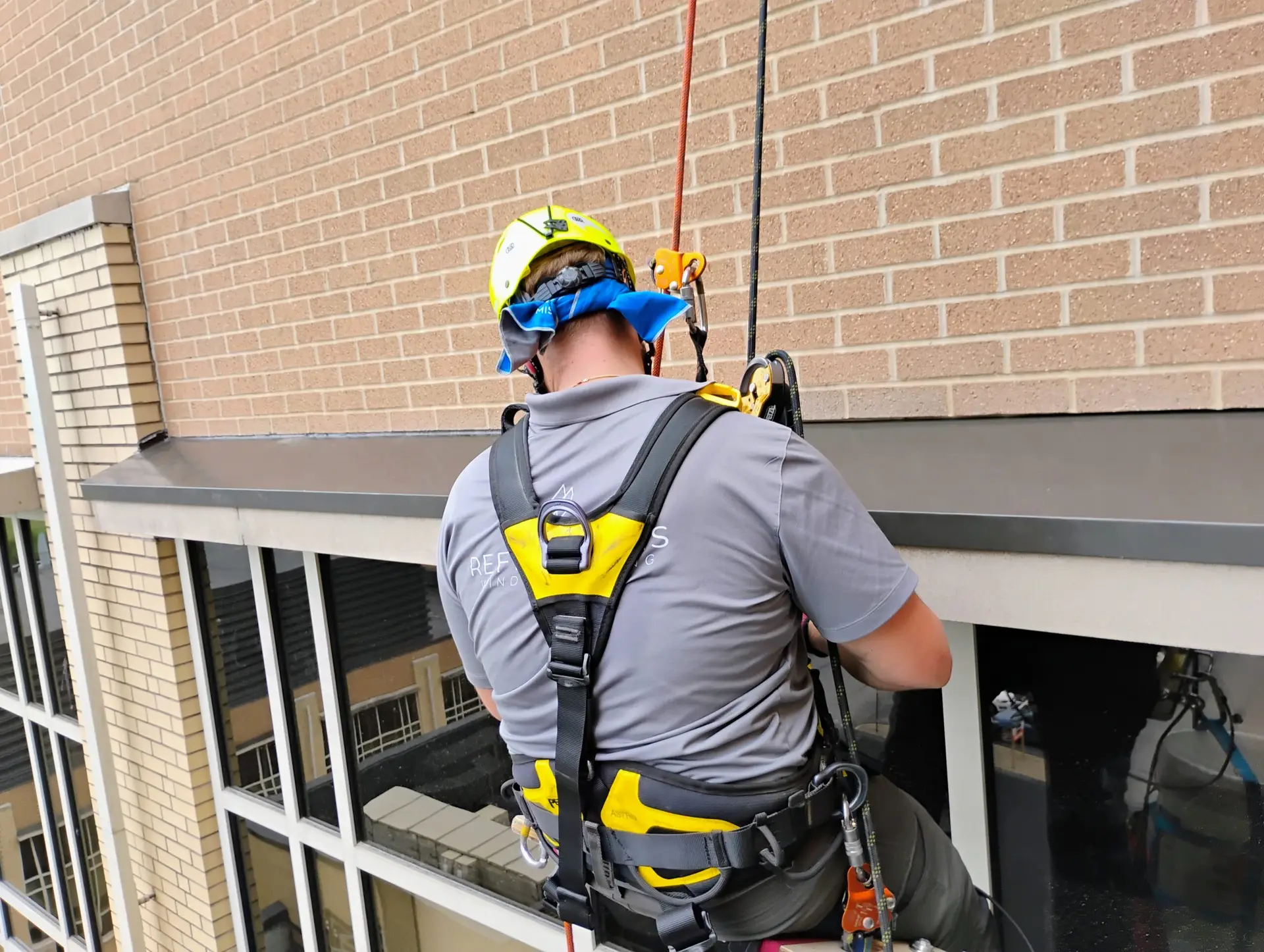 Window washer wearing a safety harness rappelling down the side of a high-rise brick building