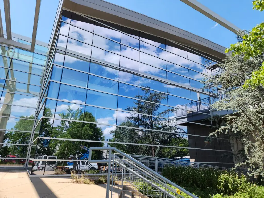 Modern glass building exterior with reflective clean windows, outdoor stairs, and landscaping