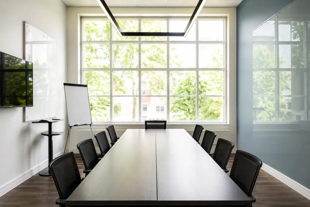 Conference room with a long table, chairs, and a large clean window overlooking trees