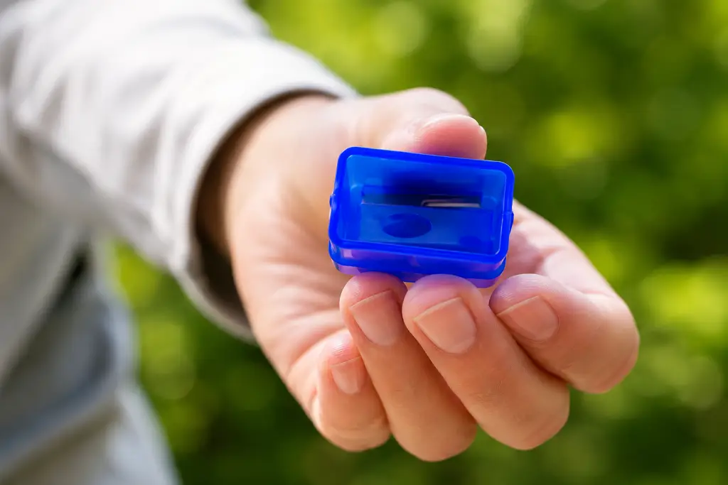 Close-up of an open hand holding a small blue handheld window-cleaning blade tool against a green outdoor background