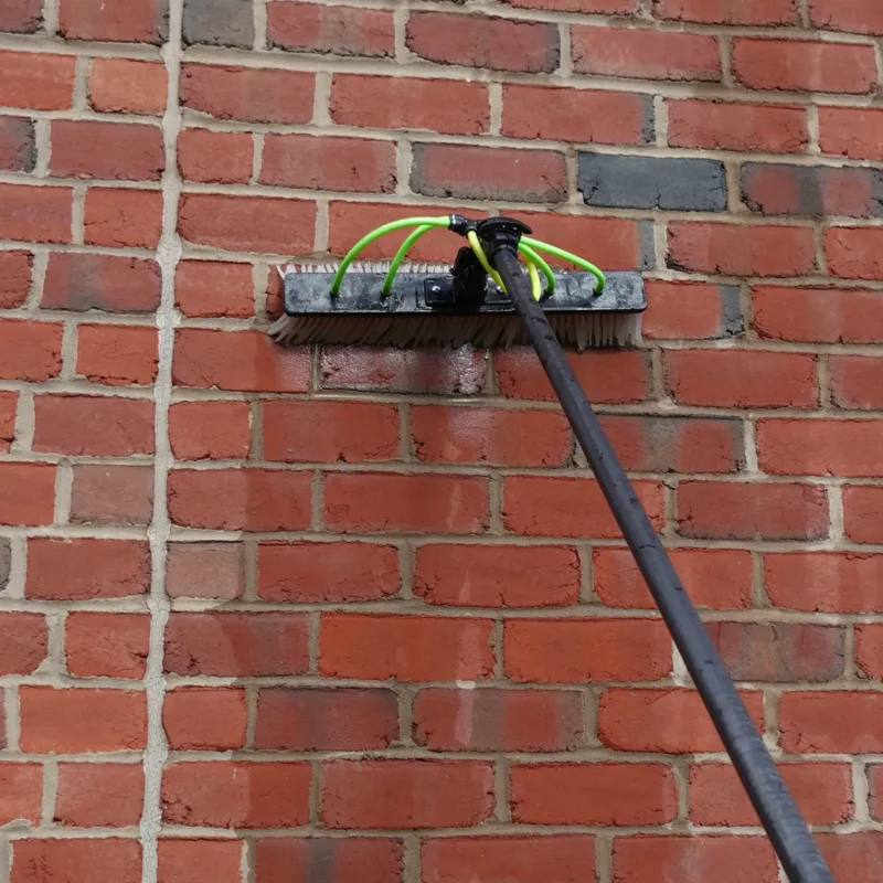 Water-fed pole brush with green hoses pressed against a brick wall for window washing